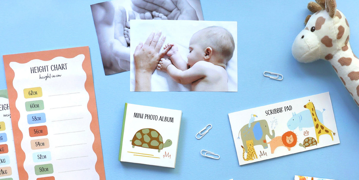 Collection of baby products including a height chart, photo album, and scribble pad on a blue background.